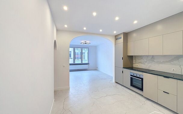Bij het betreden van dit volledig gerenoveerde appartement wordt u verwelkomd in een stijlvolle inkomhal met een elegante, afgeronde deuropening.
Direct aan de inkom bevindt zich een bureauruimte met parketlaminaat en een gloednieuw raam, ideaal voor thui