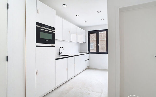 Stap binnen in dit smaakvol afgewerkte appartement, gelegen in een klassevol gerenoveerd gebouw op wandelafstand van het centrum van Edegem.
De inkomhal biedt directe toegang tot de moderne keuken, volledig uitgerust met hoogwaardige Siemens-toestellen 
