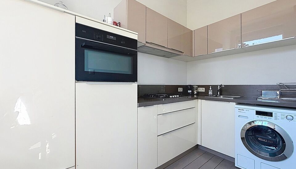 Charmant instapklaar appartement op de 2e verdieping met aangenaam open uitzicht. Inkomhal met vestiairekast. Lichtrijke woonkamer (ca. 22m&sup2;) op authentieke plankenvloer en een schouwelement. Aansluitend de half open keuken voorzien van gasfornuis, dampk