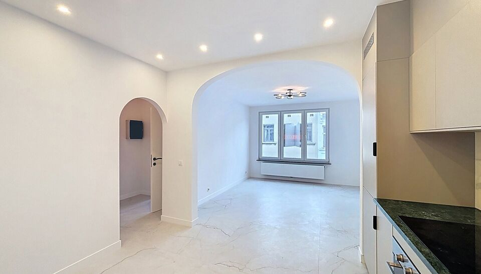 Bij het betreden van dit volledig gerenoveerde appartement wordt u verwelkomd in een stijlvolle inkomhal met een elegante, afgeronde deuropening.
Direct aan de inkom bevindt zich een bureauruimte met parketlaminaat en een gloednieuw raam, ideaal voor thui