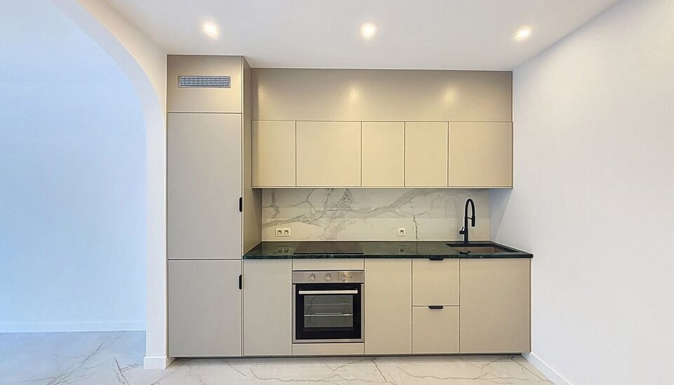 Bij het betreden van dit volledig gerenoveerde appartement wordt u verwelkomd in een stijlvolle inkomhal met een elegante, afgeronde deuropening.
Direct aan de inkom bevindt zich een bureauruimte met parketlaminaat en een gloednieuw raam, ideaal voor thui