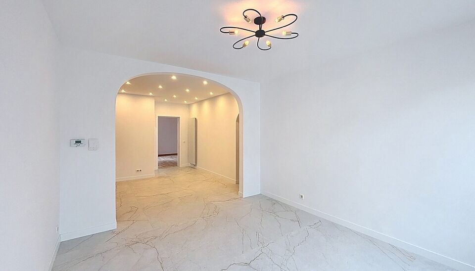 Bij het betreden van dit volledig gerenoveerde appartement wordt u verwelkomd in een stijlvolle inkomhal met een elegante, afgeronde deuropening.
Direct aan de inkom bevindt zich een bureauruimte met parketlaminaat en een gloednieuw raam, ideaal voor thui