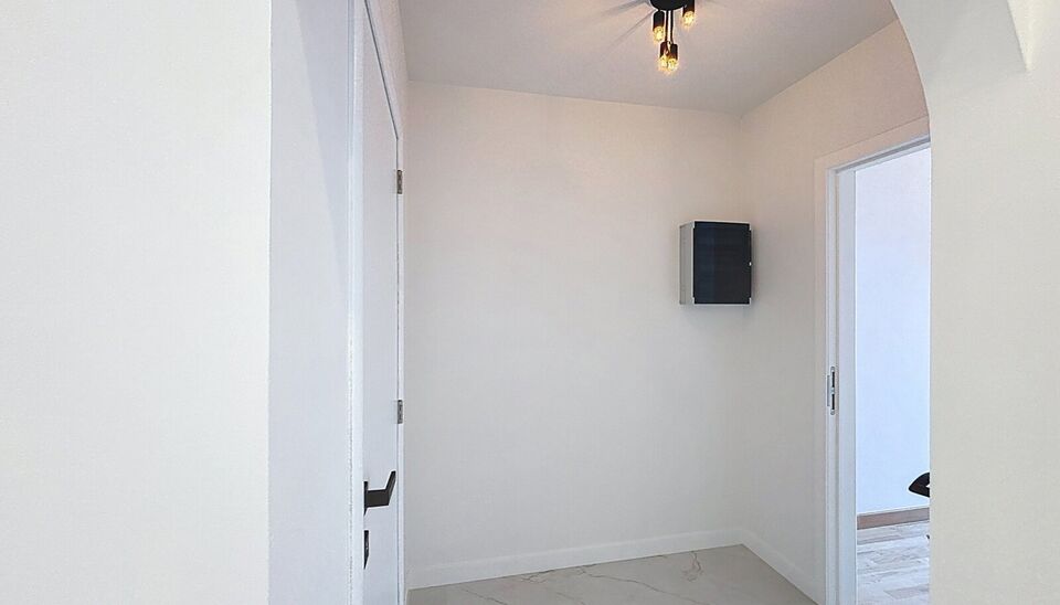 Bij het betreden van dit volledig gerenoveerde appartement wordt u verwelkomd in een stijlvolle inkomhal met een elegante, afgeronde deuropening.
Direct aan de inkom bevindt zich een bureauruimte met parketlaminaat en een gloednieuw raam, ideaal voor thui