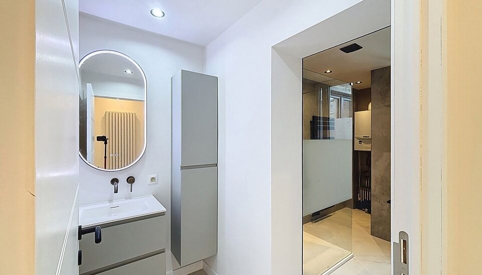 Bij het betreden van dit volledig gerenoveerde appartement wordt u verwelkomd in een stijlvolle inkomhal met een elegante, afgeronde deuropening.
Direct aan de inkom bevindt zich een bureauruimte met parketlaminaat en een gloednieuw raam, ideaal voor thui
