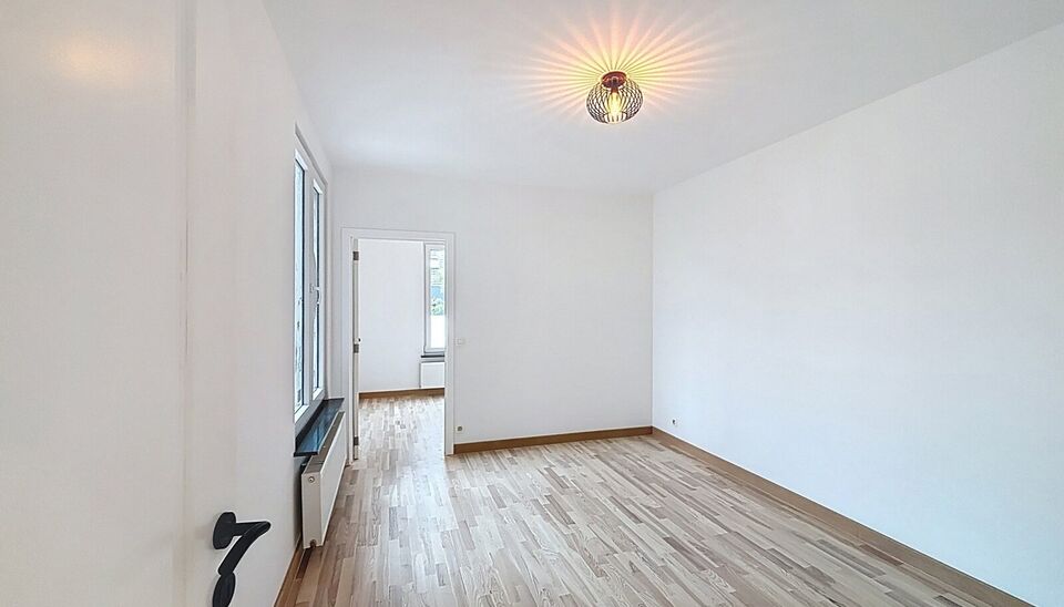 Bij het betreden van dit volledig gerenoveerde appartement wordt u verwelkomd in een stijlvolle inkomhal met een elegante, afgeronde deuropening.
Direct aan de inkom bevindt zich een bureauruimte met parketlaminaat en een gloednieuw raam, ideaal voor thui