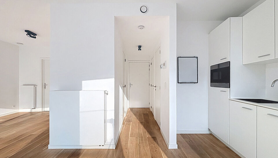 Het appartement bevindt zich op de zesde verdieping, achteraan in residentie KPlaza, een modern, energiezuinig en stijlvol nieuwbouwproject dat werd opgeleverd in 2019. Bij het betreden van de leefruimte valt meteen de mooie parketvloer op, evenals de kwa